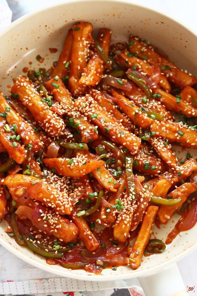 Honey glazed chili potato dish topped with sesame seeds and vegetables